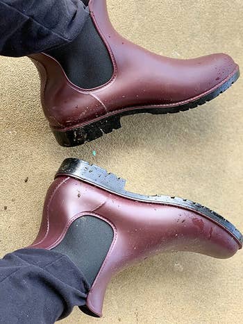reviewer wearing the maroon boots, which have some water droplets on them