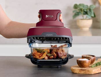 Air fryer successful use, cooking nutrient and potatoes. User's manus holding the fryer lid. Kitchen mounting with spices nearby. Ideal for speedy meals