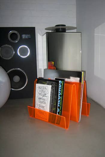 Stylish orange magazine rack holding vinyl records next to a modern speaker setup in a minimalist room