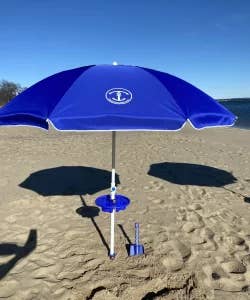 Blue beach umbrella with a stand and shovel on sandy shore. No persons visible