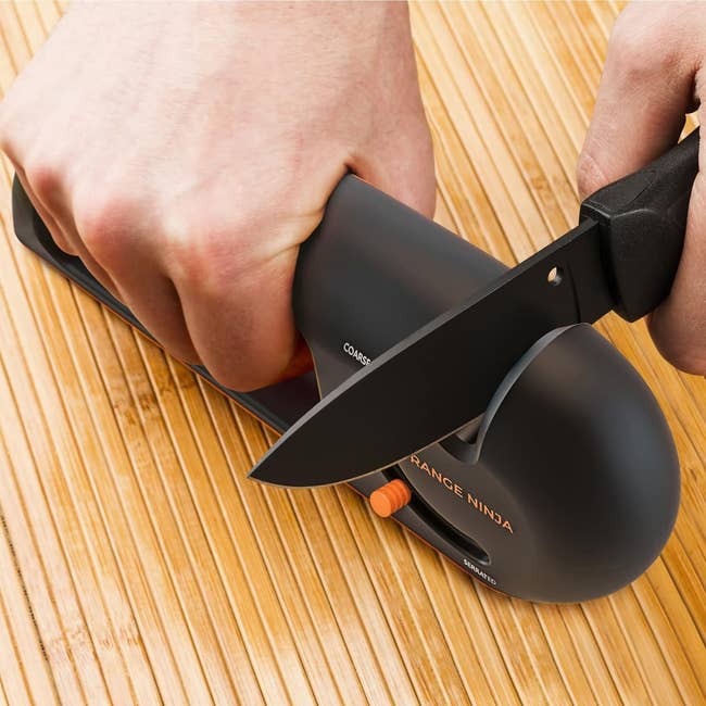 Hand using a manual knife sharpener on a chef's knife, placed on a wooden surface