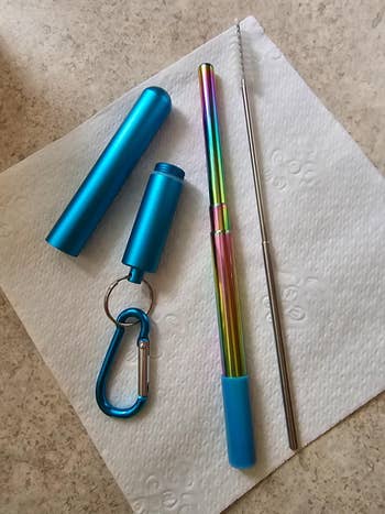 Collapsible reusable straw with a rainbow decorativeness  and bluish  lawsuit  connected  a napkin; includes a cleaning brushwood  and carabiner for portability