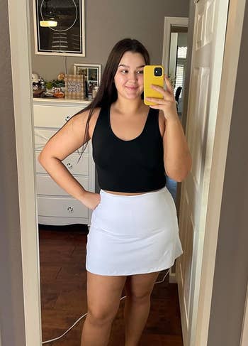reviewer in a mirror selfie wearing a black tank top and a white tennis skirt