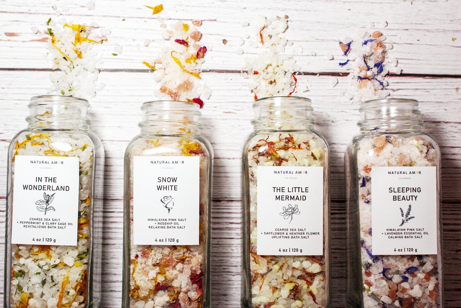 Colorful bath salts in transparent containers themed to fairy tales like Snow White, The Little Mermaid, Alice in Wonderland, and Sleeping Beauty