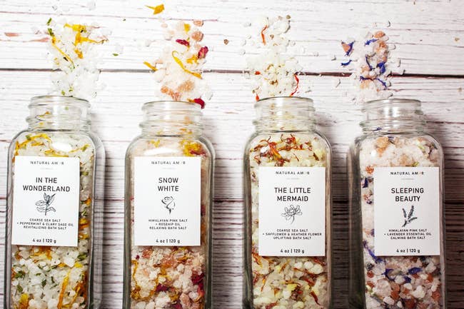 Colorful bath salts in transparent containers themed to fairy tales like Snow White, The Little Mermaid, Alice in Wonderland, and Sleeping Beauty 