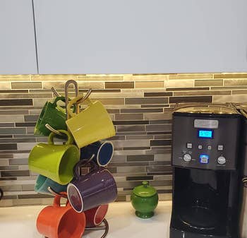 reviewer photo of colorful mugs on mug holder next to coffee m achine