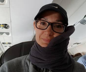 reviewer photo of themselves wearing the gray trtl pillow on a plane