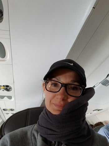 reviewer photo of themselves wearing the gray trtl pillow on a plane