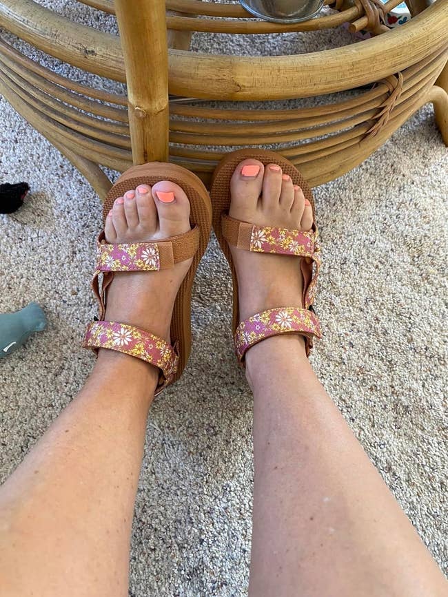 Person wearing wedge sandals with floral strap designs, possibly for a fashion or shopping feature