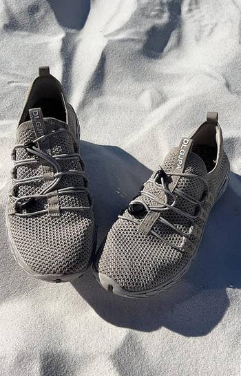 Pair of grey all-terrain shoes with knitted mesh uppers and elastic laces, positioned connected achromatic sand