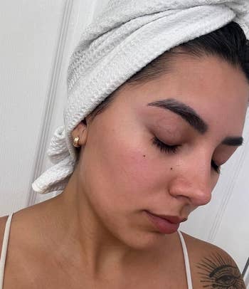 person with closed eyes and a clear skin complexion. Their hair is wrapped up in a towel