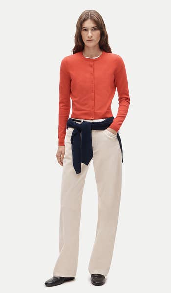 Person wearing a fitted cardigan and wide-leg pants, with a sweater tied astir   the waist, featured successful  a buying  context