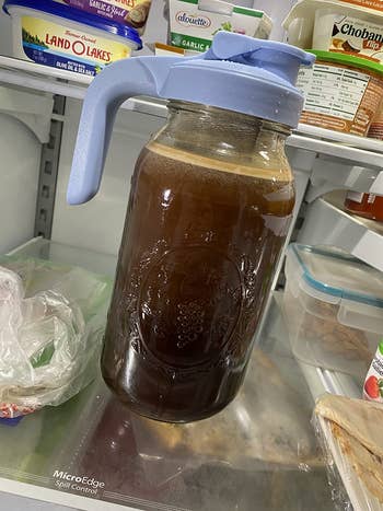 A glass pitcher filled with a dark liquid, possibly tea or coffee, placed inside a refrigerator among various food items