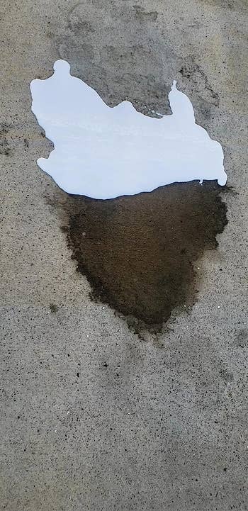 reviewer photo of the white stain-removing fluid on part of a dark oil stain on concrete