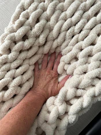 A hand presses into a plush, thickly woven, soft-textured blanket. Perfect for cozying up or home decor. Ideal for shoppers seeking comfort items