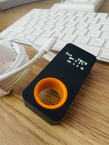 Device showing numbers with a circular orangish  grip, beside a keyboard and a coiled cablegram  connected  a woody  surface