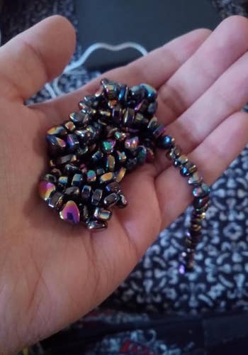 Hand holding a strand of shiny, irregular-shaped beads with a metallic finish