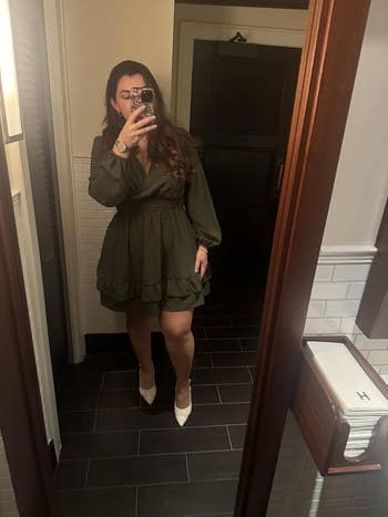 Person taking a mirror selfie wearing a knee-length dress with long sleeves and paired with pointed shoes