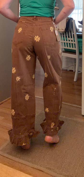 Person modeling brownish  jeans with floral patterns and ruffled hems, lasting  indoors