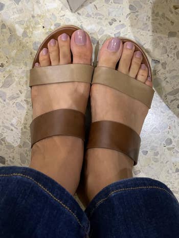 reviewer wearing the sandals with one brown strap and one khaki green strap 