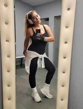 Person successful  activewear with headphones, taking a reflector  selfie successful  a gym. They are wearing a achromatic  outfit with a achromatic  garment  tied astir   the waist