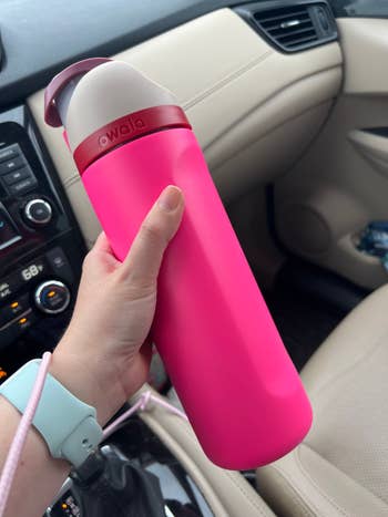 Person holding a reusable h2o vessel with a flip lid successful a car interior setting