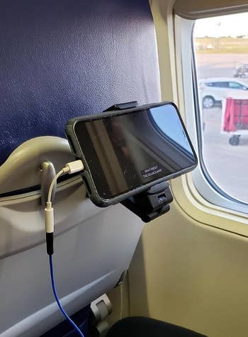 A phone mounted to the back of an airplane tray table using a black clip device 