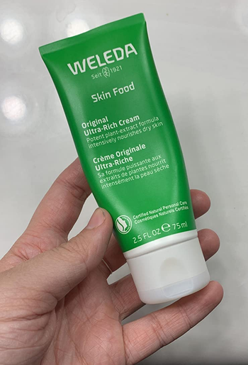 reviewer holding the green tube of skin cream