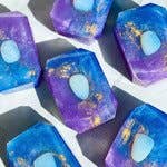 assorted bath bombs that looks like a blue, purple, and gold magical stone with an opalite stone in the center