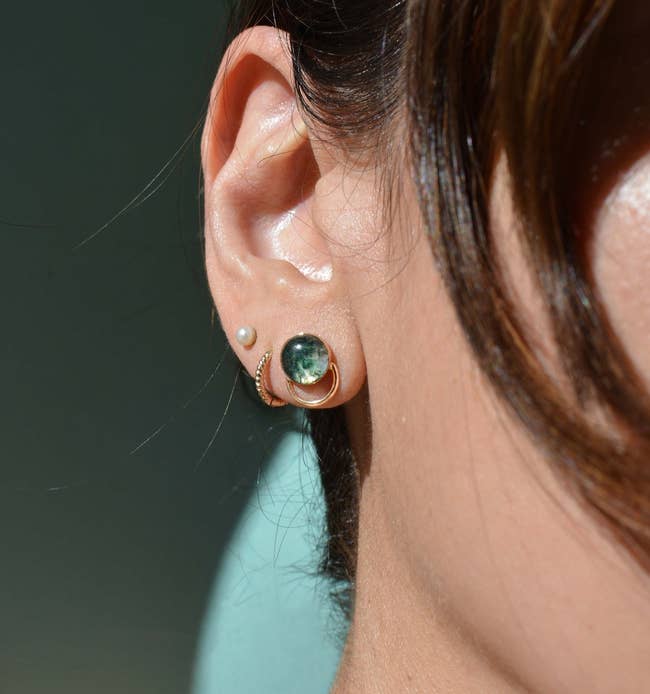 Close-up of a person's ear wearing a pearl stud and a hoop earring with a green gemstone
