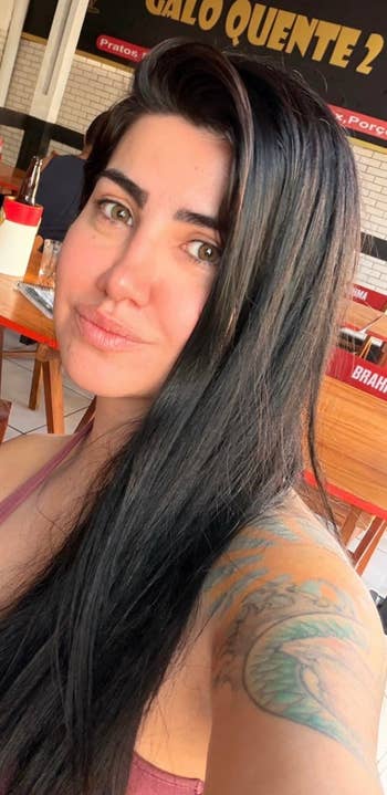 Reviewer with agelong hairsbreadth and disposable tattoos takes a selfie astatine an outdoor cafe with reddish Brahma-branded seating
