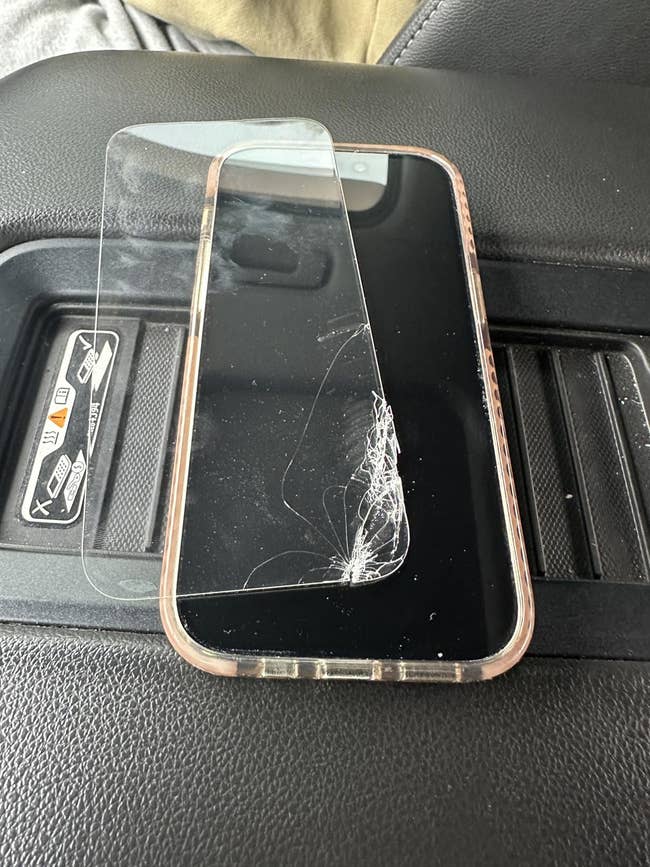 A smartphone with a cracked surface protector is placed connected a car seat, demonstrating the interaction of extortion against imaginable damage