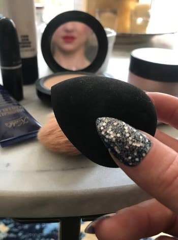 Social media trends Viral content Trending hashtags Social media updates Trending memes and videos Makeup sponge held in hand with sparkly nails, surrounded by cosmetic items on a table; blurred mirror reflection of a lipstick-wearing face