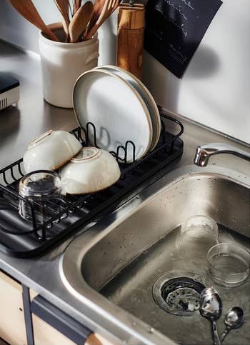 Clean dishes on a drying rack next to a kitchen sink with water and utensils