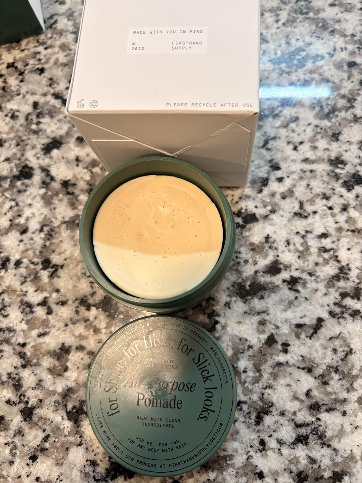 Open jar of Firsthand Supply All-Purpose Pomade on a countertop, showing product texture and packaging nearby