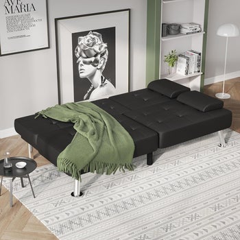 the black faux leather futon sofa in down position with blanket