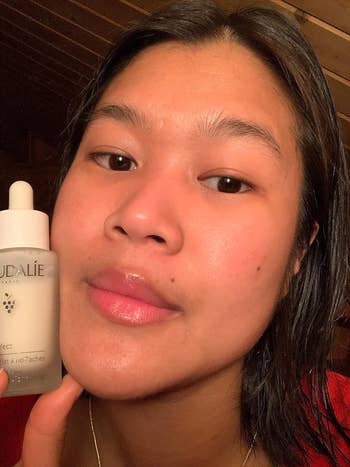 The same reviewer holding up the bottle of serum while showing their clear, hydrated skin