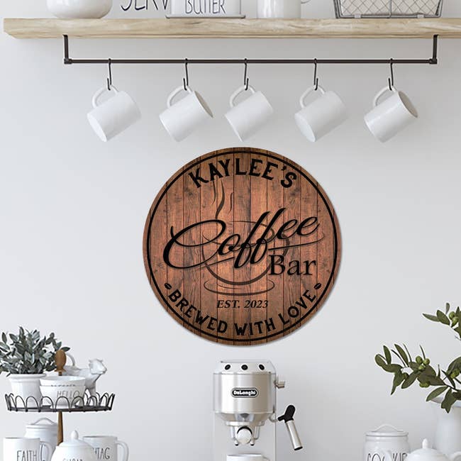 Custom wooden 'Kaylee's Coffee Bar' sign with script font, hanging in a kitchen with mugs and a coffee maker