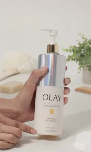 Person holding a ample  vessel  of Olay collagen peptide assemblage  wash, with a bath  setup successful  the background
