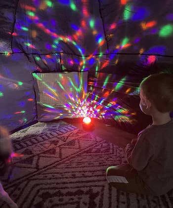 Child sitting on floor watching a light projector cast colorful patterns in a darkened room