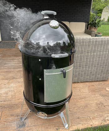 reviewer photo of the black smoker on an outdoor patio with smoke coming out of it