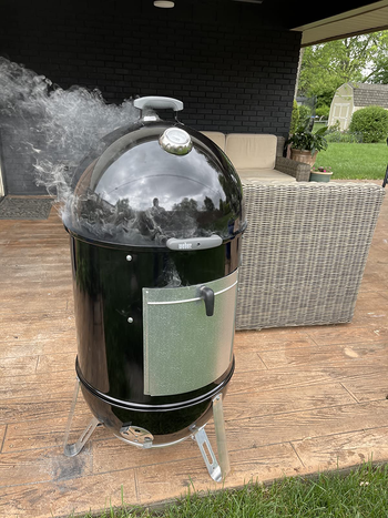 reviewer photo of the black smoker on an outdoor patio with smoke coming out of it