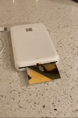 A compact Kodak photograph  printer outputs an representation  connected  a countertop
