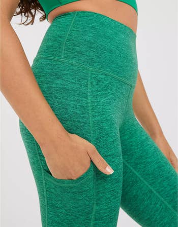 close-up of model putting their hand in the pocket of their green leggings
