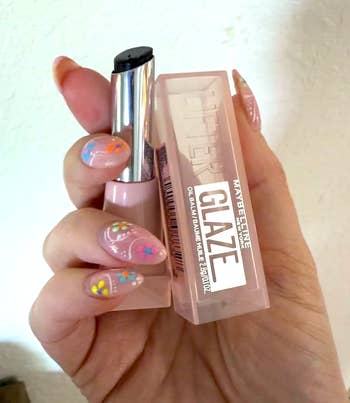 Hand holding Maybelline lip product with floral nail art design