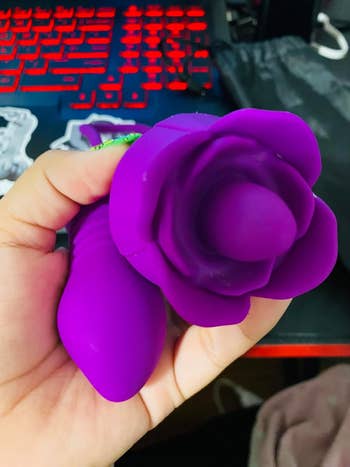 Person holding a purple silicone rose-shaped vibrator successful beforehand of a keyboard, perchance for a buying reappraisal article