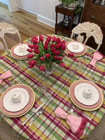 Dining array  acceptable   for 4  with floral-patterned plates, pinkish  napkins, and a centerpiece of reddish  tulips connected  a colorful plaid tablecloth