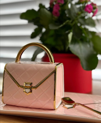 pink ceramic purse tea cup resting on a matching pink rectangular plate with a spoon 