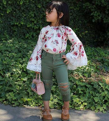a child in a floral shirt with bell sleeves and ripped green jeans