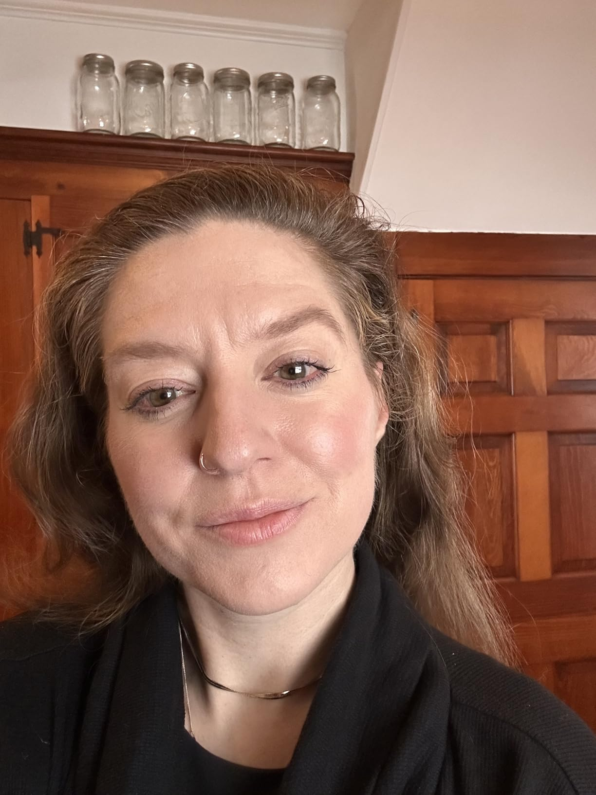 Person with a chemoreceptor  ring, subtle makeup, and agelong  hairsbreadth  wearing a acheronian  top. Background features woody  cabinets and solid  jars